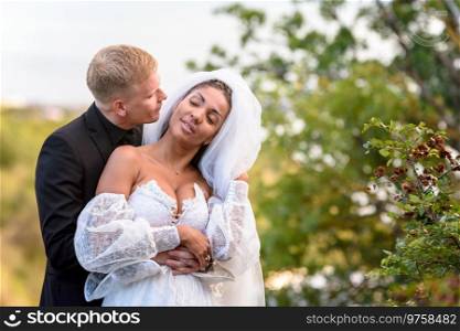 Happy newlyweds hug against the backdrop of a beautiful mountain landscape, the guy kisses the girl who has closed her eyes