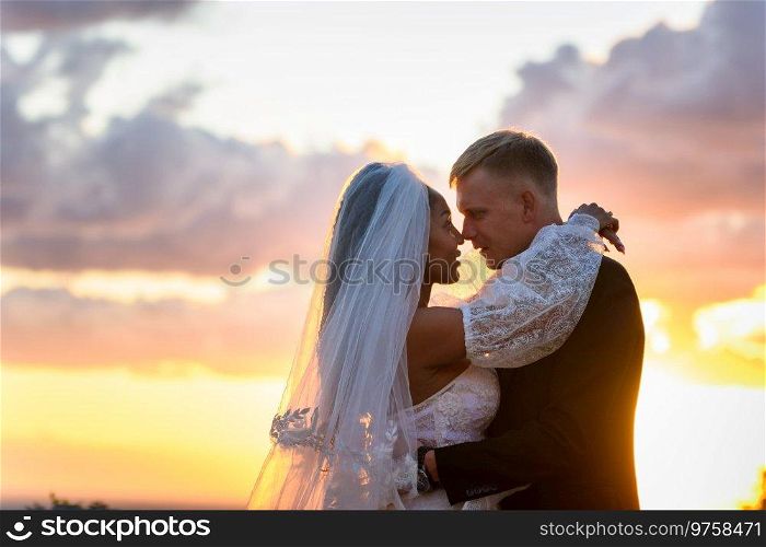 Happy newlyweds hugging against the sky in the rays of the setting sun