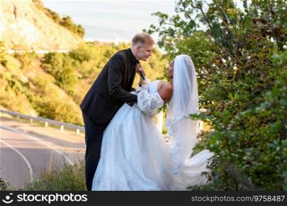 Happy newlyweds kiss against the backdrop of a beautiful mountain landscape, the girl holds the guy by the tie