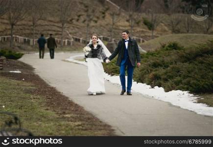 Happy newlyweds walking on the road at winter park