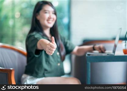 Happy of asian freelance people business female Abstract blur with focus show showing thumbs up working with laptop computer in coffee shop like the background,communication concept