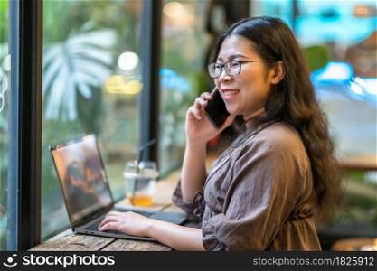 Happy of asian freelance people business female hold pick up smartphone casual working with laptop computer with coffee cup and smartphone in coffee shop like the background,communication concept
