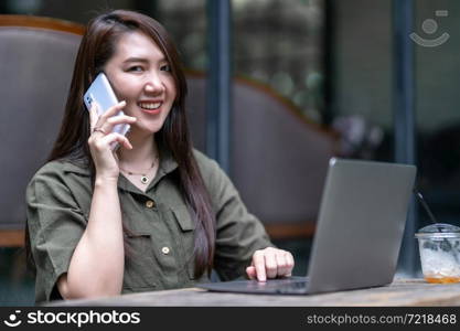 Happy of asian freelance people business female hold pick up smartphone casual working with laptop computer with coffee cup and smartphone in coffee shop like the background,communication concept