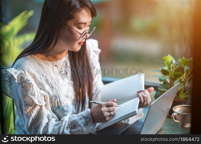 Happy of asian freelance people Businesswoman Taking written Notes to on notebook casual working with laptop computer with a coffee cup mug and smartphone at the cafe,Business Lifestyle