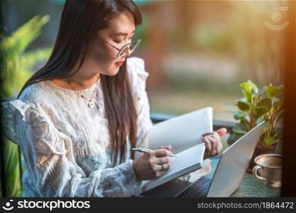 Happy of asian freelance people Businesswoman Taking written Notes to on notebook casual working with laptop computer with a coffee cup mug and smartphone at the cafe,Business Lifestyle