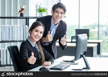 Happy of businesswoman and businessman partners showing thumbs up discussing positive adult business working together with computer on wooden table and ideas at meeting in office background.