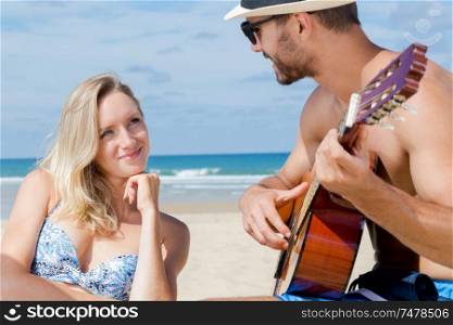 happy of man and woman playing guitar on the beach