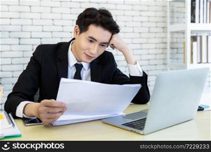 Happy of successful asian young businessman have stressed see a the document business plan and laptop computer on wooden table In the office room background.