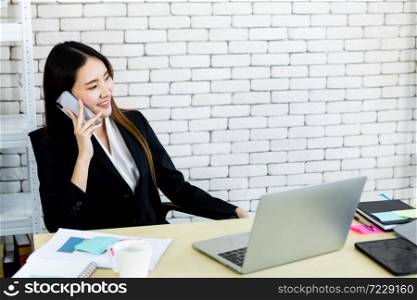 Happy of successful asian young businesswoman hold pick up smartphone working with laptop computer in on White wooden table in white wall office background