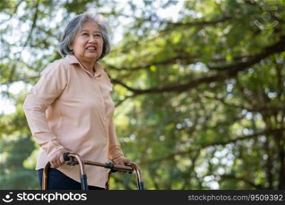 Happy old elderly Asian woman uses a walker for osteoarthritis rehabilitation physiotherapy in park.  Concept of happy retirement With care from a caregiver and Savings and senior health insurance