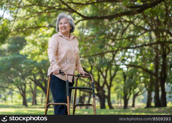 Happy old elderly Asian woman uses a walker for osteoarthritis rehabilitation physiotherapy in park.  Concept of happy retirement With care from a caregiver and Savings and senior health insurance