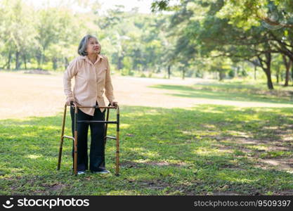 Happy old elderly Asian woman uses a walker for osteoarthritis rehabilitation physiotherapy in park.  Concept of happy retirement With care from a caregiver and Savings and senior health insurance