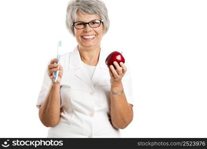 Happy old female doctor holding a apple and a toothbrush isolated on white