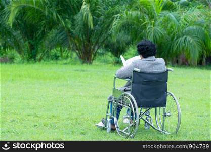 Happy old woman in a wheelchair reading a book in the garden.