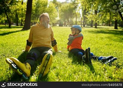Happy overjoyed man and boy rollerskaters rest on grass filed in park. Young and adult people having active leisure activity and fun sports time together. Happy overjoyed man and boy rollerskaters rest on grass filed in park