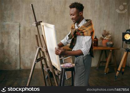 Happy painter prepares easel with canvas in art studio. Male artist draws at his workplace, creative master works in workshop. Happy painter prepares easel with canvas