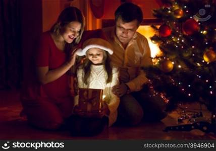 Happy parents and cute daughter looking inside of Christmas present