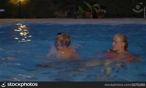 Happy parents and little son having fun in the pool at night. Father jumping with kid and mother splashing water
