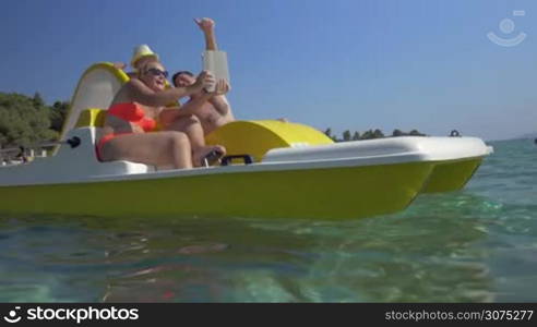 Happy parents and son taking selfie with touch pad as they sailing on pedal boat in the sea. Family summer vacation