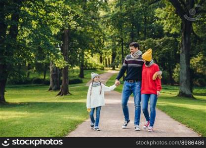 Happy parents feel proud of their small beautiful daughter, have walk together in park, enjoy autumn weather. Family have rest during weekends across green park or forest. Parents and childhood