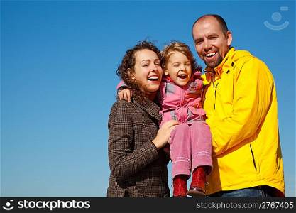 Happy parents together with daughter on hands bright sunny day against blue sky.