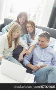 Happy parents with daughters using laptop in living room