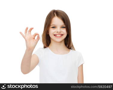 happy people and gesture concept - smiling little girl in blank white t-shirt showing ok gesture. little girl in white t-shirt showing ok gesture