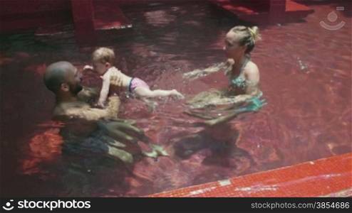 Happy people, family, father, mother, child, baby in swimming pool. Mom and dad helping daughter, little girl, infant swim. Fun, leisure, recreation, lifestyle, parenthood. 8of8