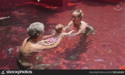 Happy people, family, mother, child, baby, swimming pool. Mom helping daughter, little girl swim, with grandmother, grandma in water. Child rearing. Sequence, 4of8