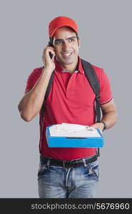 Happy pizza delivery man answering mobile phone against gray background