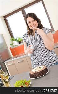 Happy plus size woman with white wine, chocolate cake and cream in modern kitchen