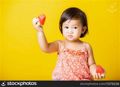 Happy portrait Asian baby or kid cute little girl attractive laugh smile wearing t-shirt playing holds cut watermelon fresh for eating, studio shot isolated on yellow background, healthy food and summer concept