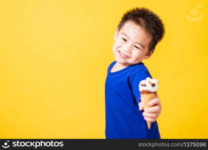 Happy portrait Asian child or kid cute little boy attractive laugh smile playing holds and eating sweet chocolate ice cream waffle cone, studio shot isolated on yellow background, summer concept