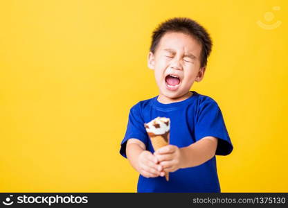 Happy portrait Asian child or kid cute little boy attractive laugh smile playing holds and eating sweet chocolate ice cream waffle cone, studio shot isolated on yellow background, summer concept