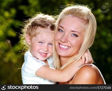 Happy portrait of the smiling and beautiful mother and little daughter - outdoors