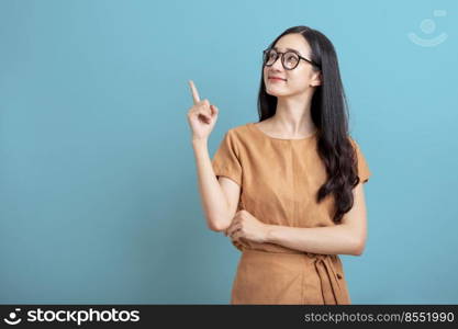 Happy Portrait smiling young asian woman isolated on blue background , Beautiful asian female pointing finger upward on blue background