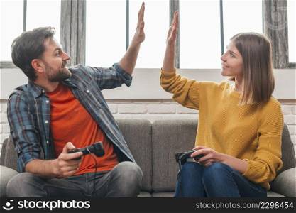happy portrait young couple sitting sofa giving high five each other while playing video game