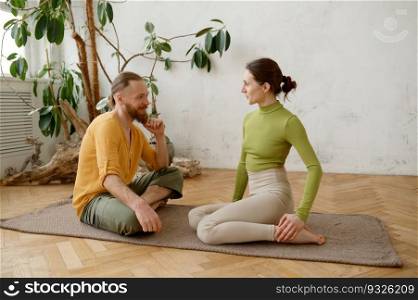 Happy positive couple speaking after active yoga training sharing expressions sitting on mat at home living room. Happy positive couple speaking after active yoga training