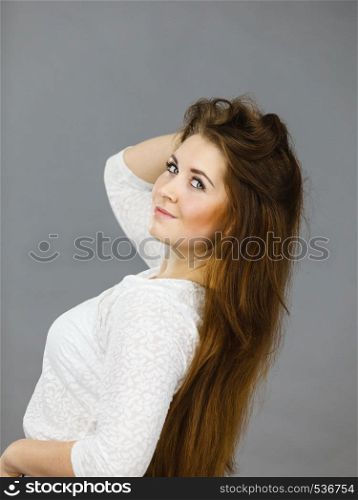 Happy positive woman with long brown hair presenting her healthy hairdo. Haircare concept. Studio shot on grey backgorund.. Happy positive woman with long brown hair