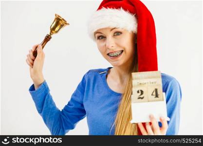Happy positive young teenage woman wearing Santa Claus christmas hat holding calendar with 24 december date and bell. Woman and christmas calendar with bell