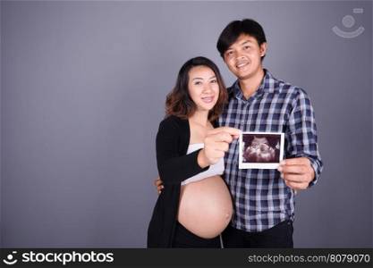 happy pregnant and husband showing ultrasound image on gray wall background
