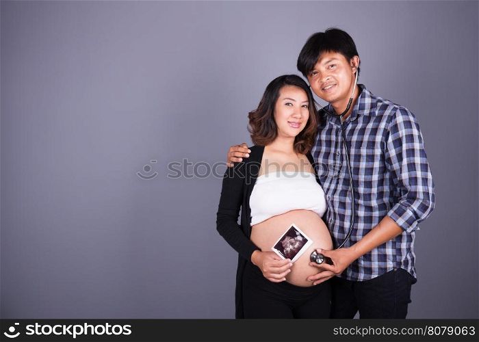 happy pregnant and husband with stethoscope and ultrasound image on gray wall background