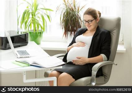 Happy pregnant businesswoman posing in chair at office