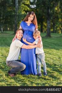 Happy pregnant family of three expecting new baby. Father and mother with little boy hugging outdoors.