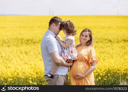Happy pregnant family with little daughter spending time together in a yellow rapeseed field on summer day.. Happy pregnant family with little daughter spending time together in a yellow rapeseed field on summer day