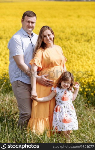 Happy pregnant family with little daughter spending time together in a yellow rapeseed field on summer day.. Happy pregnant family with little daughter spending time together in a yellow rapeseed field on summer day