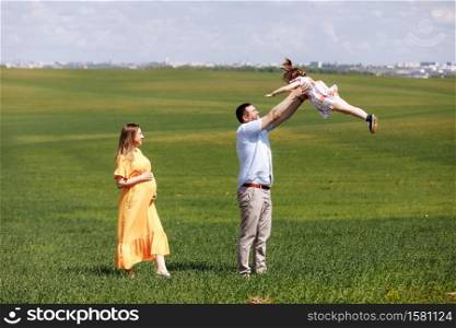 Happy pregnant family with little daughter spending time together in sunny green field on summer day.. Happy pregnant family with little daughter spending time together in sunny green field on summer day