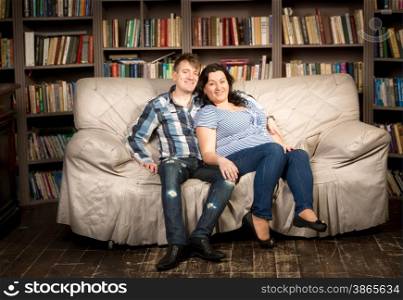 Happy pregnant woman and husband posing on couch at living room