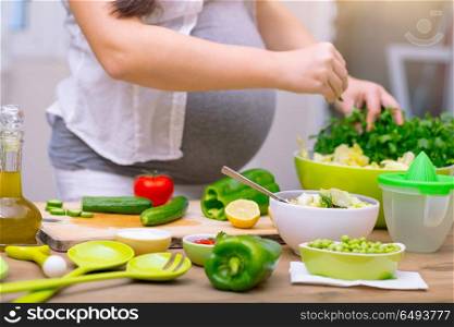 Happy pregnant woman cooking at home, doing fresh green salad, eating many different vegetables during pregnancy, healthy pregnancy concept. Healthy pregnancy concept