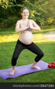 Happy pregnant woman doing yoga on grass at park